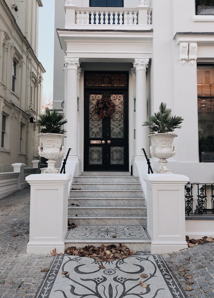 stairs-towards-closed-door-1661566 Wide-angle view of a classic luxury townhouse entrance in London featuring ornate columns and potted plants.